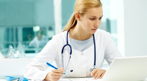 Image shows a lady nurse with stethoscope writing.