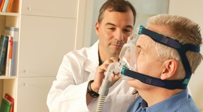 Pulmologist/doctor showing sleep apnea patient  CPAP device and sleep mask used for home sleep therapy.